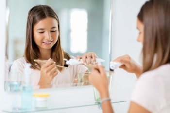 dental care, hygiene and people concept - happy smiling teenage girl with toothbrush brushing teeth at bathroom. teenage girl with toothbrush brushing teeth