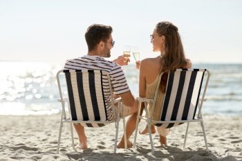 leisure, relationships and people concept - happy couple drinking champagne sitting in folding chairs on summer beach. happy couple drinking champagne on summer beach