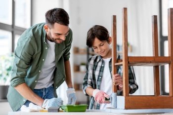 renovation, diy and home improvement concept - father and son in gloves with paint roller painting old wooden table in grey color. father and son painting old table in grey color