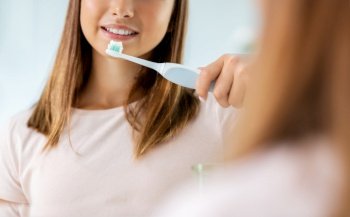 dental care, hygiene and people concept - happy smiling teenage girl with electric toothbrush brushing teeth at bathroom. teen girl with electric toothbrush brushing teeth