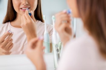 beauty and cosmetics concept - teenage girl applying lipstick and looking to mirror at home bathroom. teenage girl applying lipstick at bathroom
