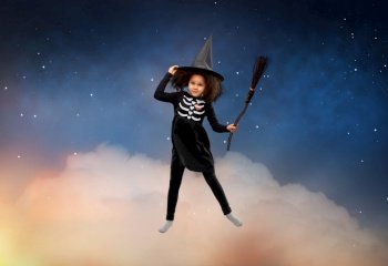 halloween, holiday and childhood concept - smiling african american girl in black costume dress and witch hat with broom over starry night sky and cloud background. girl in black witch hat with broom on halloween