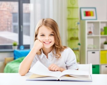 education and school concept - happy smiling student girl reading book over home background. happy smiling student girl reading book at home