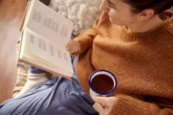 people, season and leisure concept - young woman reading book and drinking coffee at home. woman reading book and drinking coffee at home