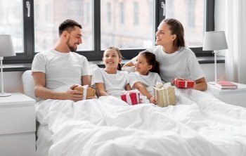 family, winter holidays and people concept - happy mother, father and two daughters in pajamas with christmas gifts in bed at home. happy family with christmas gifts in bed at home
