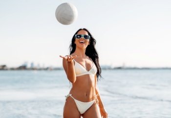 people, summer and leisure concept - happy smiling young woman in bikini swimsuit playing with volleyball on beach. woman in bikini playing with volleyball on beach