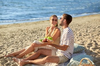 leisure, relationships and people concept - happy couple in sunglasses having picnic on summer beach. happy couple having picnic on summer beach