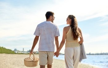 leisure, relationships and people concept - happy couple with picnic basket walking along beach. happy couple with picnic basket walking on beach