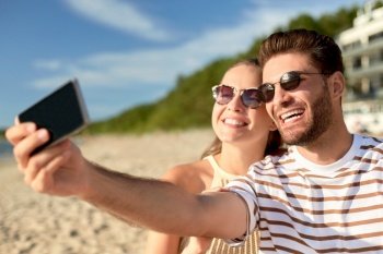 technology, leisure and people concept - happy couple taking selfie by smartphone on summer beach. happy couple taking selfie by smartphone on beach