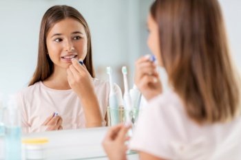 beauty and cosmetics concept - teenage girl applying lip balm and looking to mirror at home bathroom. teenage girl applying lip balm at bathroom