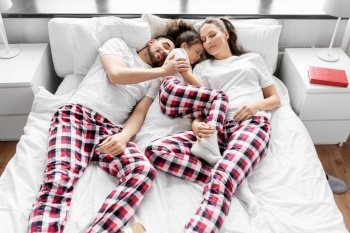 family, rest and people concept - happy little daughter, mother and father in matching pajamas sleeping in bed at home. happy family in pajamas sleeping in bed at home