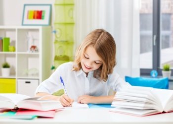 education, elementary school, learning and people concept - happy smiling girl with notebook and pen sitting at table over home background. happy smiling school girl with notebook and pen