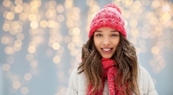 people, season and christmas concept - portrait of happy smiling teenage girl or young woman in winter over festive lights background. smiling teenage girl outdoors in winter