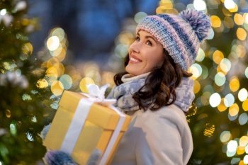 winter holidays, celebration and people concept - happy smiling woman with christmas gift over festive lights. happy woman with christmas gift over lights