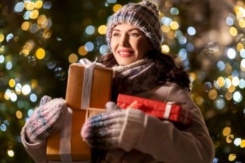winter holidays, celebration and people concept - happy smiling woman with christmas gifts over festive lights. happy woman with christmas gifts over lights