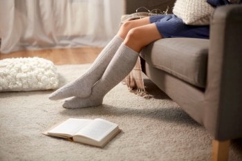 people and leisure concept - young woman in knee socks with book on floor sitting on sofa at home. woman in socks with book on floor at home