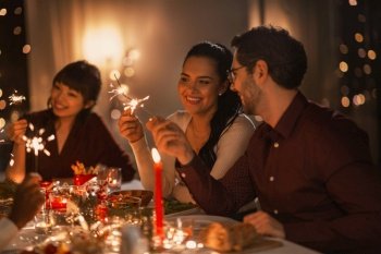 holidays and celebration concept - multiethnic group of happy friends with sparklers having christmas dinner at home. happy friends with sparklers at christmas dinner