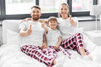 family, rest and people concept - happy mother, father and little son in matching pajamas showing thumbs up in bed in morning. happy family in pajamas in bed in morning