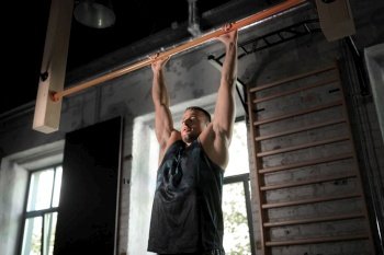 sport, fitness, exercising and people concept - man doing pull-ups on horizontal bar in gym. man exercising on bar and doing pull-ups in gym