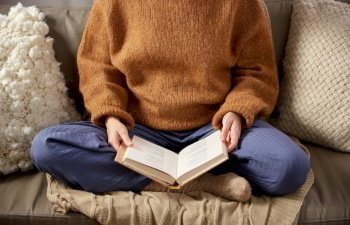 people, season and leisure concept - close up of woman in warm sweater reading book at home. woman in warm sweater reading book at home
