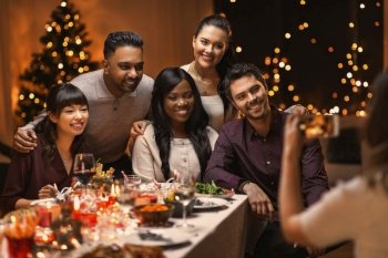 holidays, party and celebration concept - multiethnic group of happy friends having christmas dinner and photographing at home. happy friends photographing on christmas at home