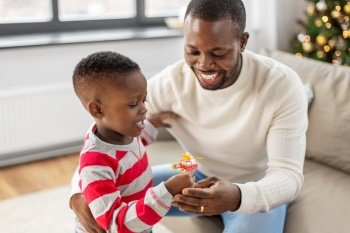 family, winter holidays and people concept - happy african american mother, father and baby son opening gift box with toy at home on christmas. african family opening christmas gift at home