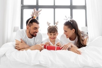 family, winter holidays and people concept - happy mother, father and little son in pajamas with christmas gift in bed in morning. family with christmas gift in bed in morning