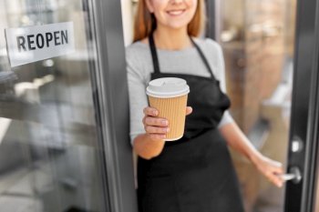 small business, reopening and service concept - close up of happy smiling woman with takeaway coffee cup and reopen banner on window or door glass. happy woman with coffee and reopen banner on door