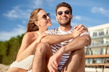 leisure, relationships and people concept - happy couple in sunglasses sitting on summer beach. happy couple sitting on summer beach