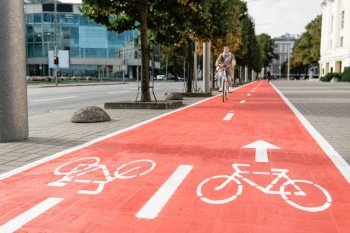 traffic, city transport and people concept - woman cycling along red bike lane with signs of bicycles and two way arrows on street. woman cycling along red bike lane road in city