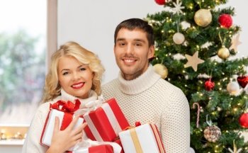winter holidays and people concept - happy couple in sweaters with gifts over christmas tree lights on background. happy couple with christmas gifts at home