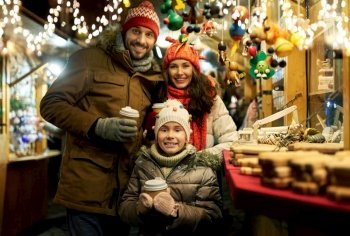 family, winter holidays and celebration concept - happy mother, father and little daughter with takeaway drinks at christmas market on town hall square in tallinn, estonia over lights. family with takeaway drinks at christmas market