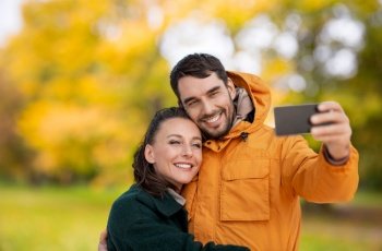 technology, season and people concept - happy couple taking selfie with smartphone over autumn park background. couple taking selfie with smartphone in autumn