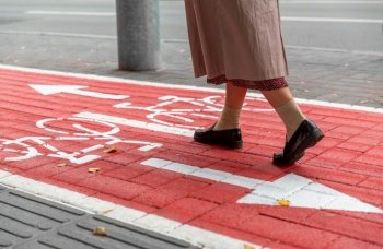 city and traffic concept - close up of woman’s feet walking along separate bike lane or red road with signs only for bicycles on street. feet walking along bike lane or road for bicycles
