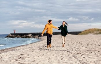 love, relationship and people concept - happy smiling couple running along autumn beach and holding hands. couple running along autumn beach