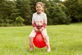 childhood, leisure and people concept - happy little girl bouncing on hopper ball at park. happy little girl bouncing on hopper ball at park