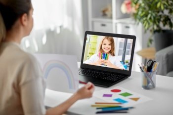education, school and distant learning concept - female art teacher with laptop computer and picture of rainbow having online class with student girl at home. art teacher having online class with student girl