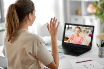 education, school and distant learning concept - female math teacher with laptop computer and earphones having online class and waving hand to student girl at home. math teacher having online class with student girl