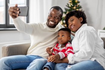 family, winter holidays and people concept - happy african american mother, father and little son taking selfie at home on christmas. african family taking selfie on christmas at home