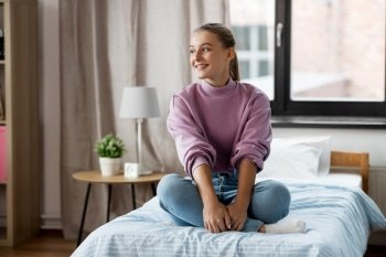 people concept - happy smiling girl sitting on bed at home. happy smiling girl sitting on bed at home