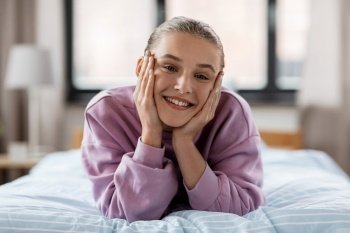 people concept - happy smiling girl lying on bed at home. happy smiling girl lying on bed at home