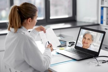 healthcare, technology and medicine concept - female doctor in white coat with laptop computer and cardiogram having video call with patient at hospital. doctor with laptop having video call at hospital