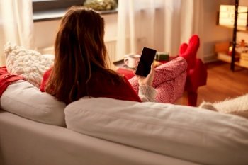 christmas, winter holidays and leisure concept - young woman using smartphone at cozy home. woman using smartphone at home on christmas
