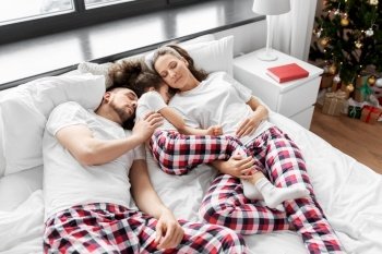 family, winter holidays and people concept - happy little daughter, mother and father in matching pajamas sleeping in bed on christmas morning. happy family sleeping in bed on christmas morning