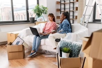 moving, people and real estate concept - happy smiling women using laptop computer and drinking coffee at new home. women using laptop and moving to new home