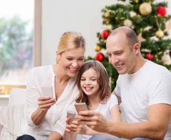 family, winter holidays and technology concept - happy mother, father and daughter with smartphones at home over christmas tree lights background. happy family with smartphones at home on christmas