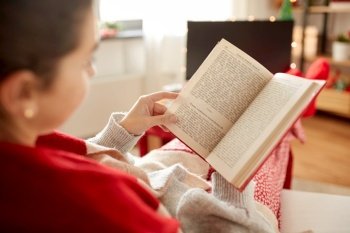 christmas, winter holidays and leisure concept - close up of young woman reading book and resting her feet on table at cozy home. young woman reading book at home on christmas