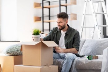 moving, people and real estate concept - happy smiling man with boxes and flower at new home. happy man unpacking boxes and moving to new home