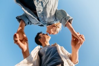 summer holidays, love and people concept - happy young couple holding hands under blue sky, from below. happy young couple holding hands under blue sky