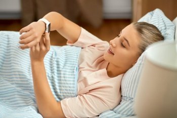 people, sleeping and rest concept - smiling girl with smart watch lying in bed at home. smiling girl with smart watch lying in bed at home